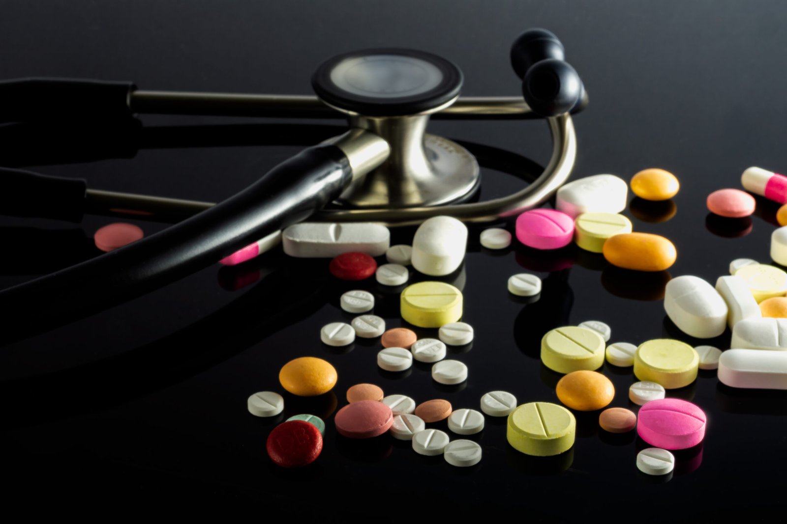 A closeup shot of a stethoscope with pills on black background