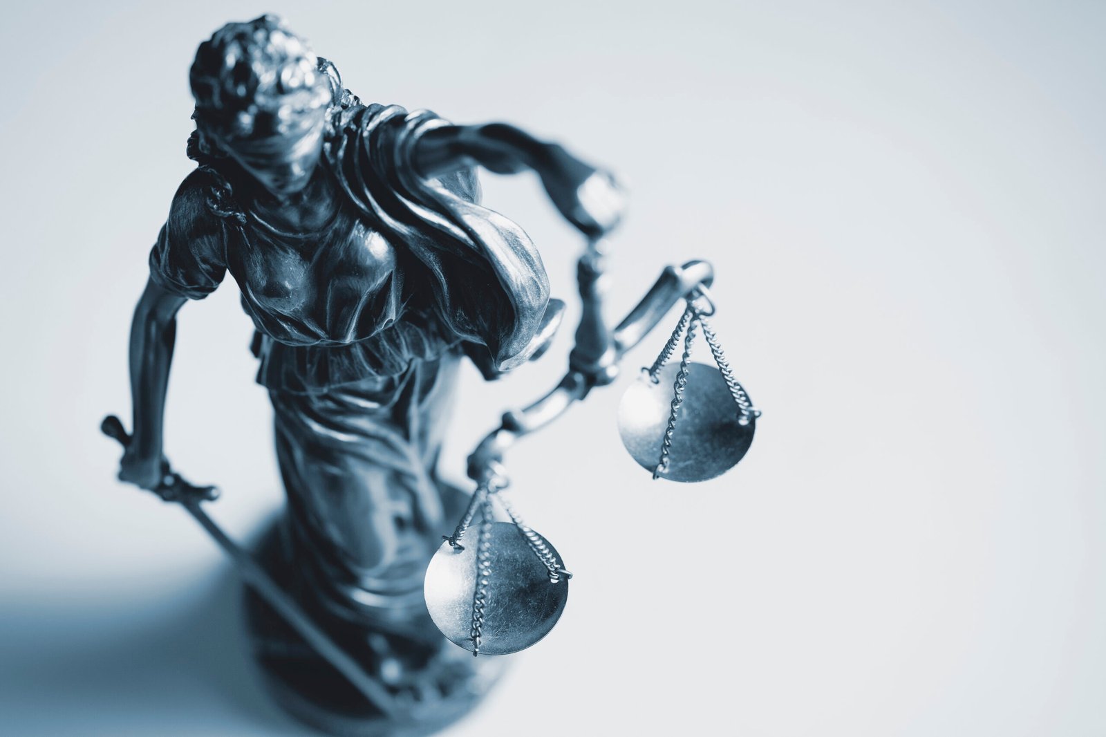 Top down view of a statue of Justice wearing a blindfold and holding a sword and the scales of Justice in a law enforcement, judicial and judgement concept over white with copy space